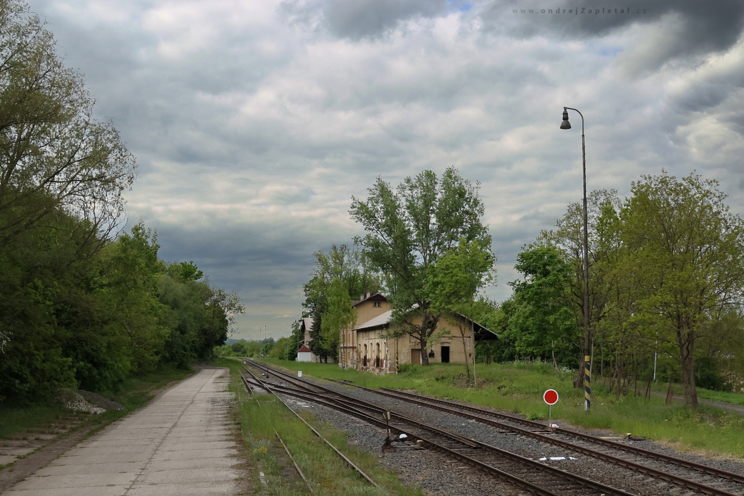 Depo na nádraží (Na fotografii:  (Průmyslová fotografie) budova, vlak, mraky, stromy)